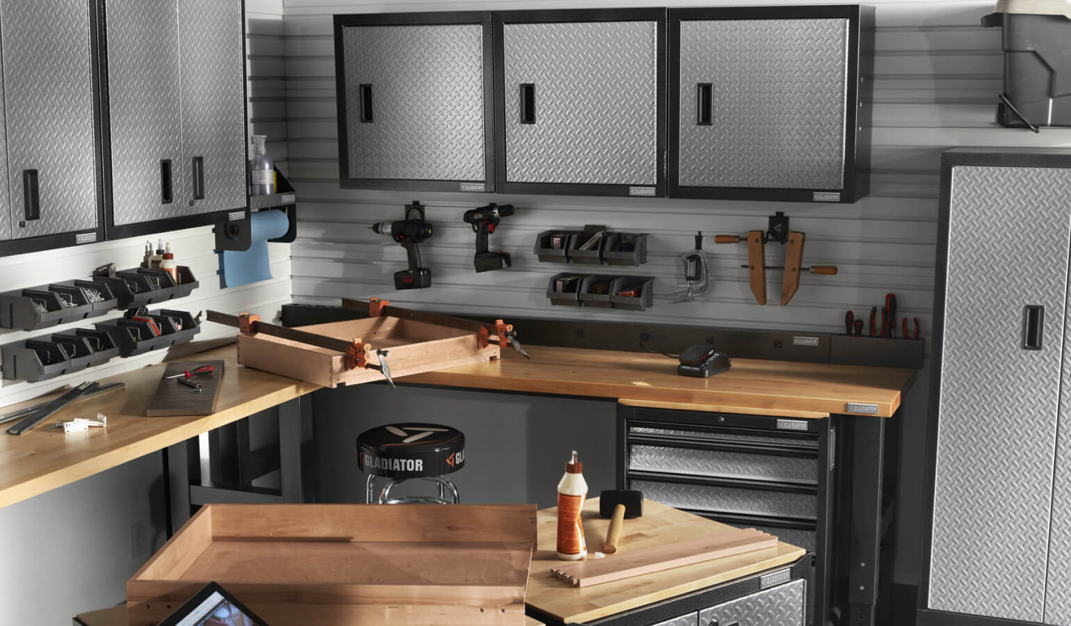 A garage woodworking space, outfitted with various Gladiator brand wall cabinets, shelves, and workbenches.